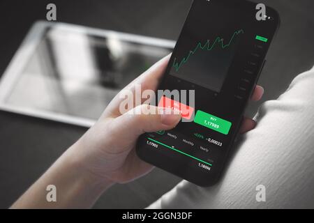 Börsenhandel zu Hause. Person, die Mobiltelefon mit Finanzgraphen für Investitionen, Kauf und Verkauf verwendet Stockfoto