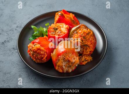 Paprika, gefüllt mit putenfleisch, Reis und Gemüse auf einem schwarzen Teller auf einem dunkelgrau-blauen Hintergrund. Stockfoto