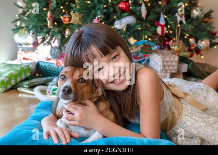 Das achtjährige Mädchen und ihr Hund vor dem Weihnachtsbaum Stockfoto