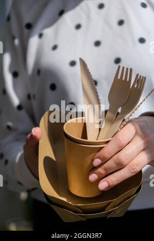 Weibliche Hände mit Holzgabeln und Pappbecher mit Tellern. Umweltfreundliches Einweggeschirr. Wird in Fast Food, Restaurants, Imbissbuden und Picknicks verwendet Stockfoto