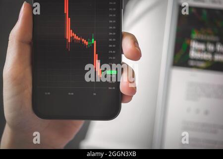 Person, die mit dem Aktienhandel beschäftigt ist. Hintergrundfoto für Unternehmen und Investitionen. Smartphone mit Finanzgraphen auf dem Bildschirm Nahaufnahme Stockfoto