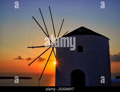 Landschaftsansicht der untergehenden Sonne über der Ägäis hinter einer traditionellen Windmühle Oia, Santorini, einer griechischen Mittelmeerinsel der Kykladen-Gruppe Stockfoto