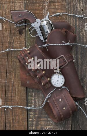 Cowboy 6 Shooter, Pistole mit Holster in Barbwire gefangen, auf Holzhintergrund. (Das alte westliche Buchcover)? Stockfoto