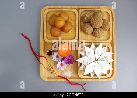 Indisches Festival Raksha bandhan. Rakhi-Thali mit Diya, Blumen und Tilak mit verschiedenen Süßigkeiten wie Gulab Jamun, Kaju katli und Churma Laddo. Stockfoto