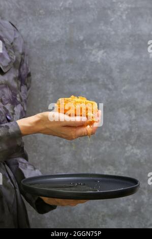 Weibliche Hand holdong frischer Honig in Honigwabe über Teller Stockfoto