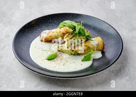 Dünnes Crepe, gefüllt mit Käse, Rucola und Spinat auf einem Teller mit cremiger Sauce Stockfoto