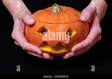 Hände halten Jack Laterne, lächelnd Halloween Kürbis mit Augen geschnitzt aus einem orangen Kürbis isoliert auf einem schwarzen Hintergrund, Vorbereitung Jack-o'-Laterne f Stockfoto