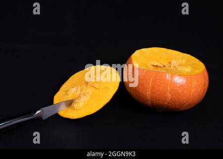 Schritt 1 Schneiden Sie die Oberseite des Kürbisses ab. Messer und Kürbis in 2 Stücke geschnitten, isoliert auf schwarzem Hintergrund, Nahaufnahme, Kopierraum. Schritt-für-Schritt-Anleitung Stockfoto