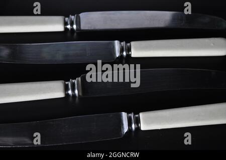 Antike Buttermesser auf schwarzem Hintergrund in einem sich wiederholenden Muster Stockfoto