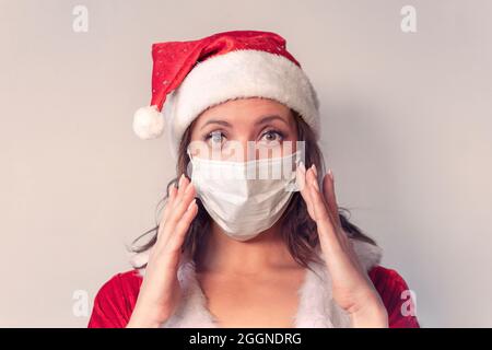Schöne junge Frau im roten Weihnachtsmann Kostüm und schützende medizinische Maske gegen Virus. Konzept der Weihnachtsfeier in covid 19 Pandemie und Stockfoto