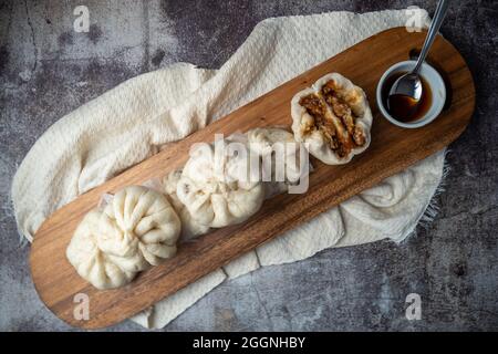 Siopao Asado, philippinisches gedünstetes Schweinebun, serviert auf einem Holztablett vor betontem Hintergrund Stockfoto