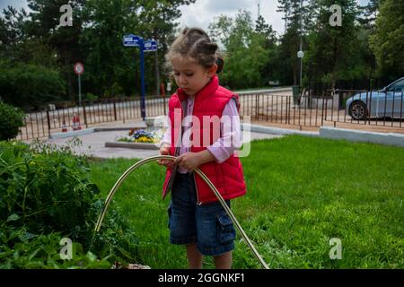 Kleines Mädchen wässert Tomaten und Pfeffer Sämlinge in ihrem Garten mit einem Gartenschlauch. Selektiver Fokus. Stockfoto