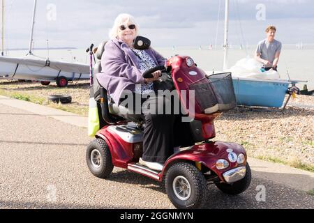 Frau mit Rollstuhl/Fahrrad genießt einen sonnigen Tag in der Stadt am Strand und beobachtet das Segelrennen in Tankerton, Kent, England Stockfoto