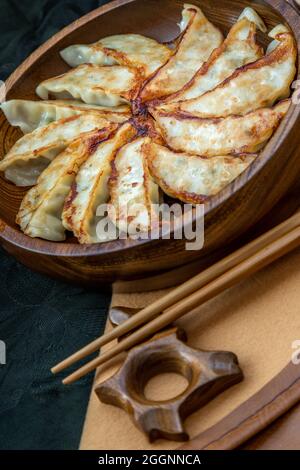 Gebratene japanische Gyoza-Knödel auf Holzschüssel serviert mit Sojasoße und Essstäbchen. Asiatisches Abendessen, ausgewählte Gerichte. Stockfoto