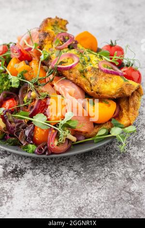 Omelette mit geschmortem Gemüse und Lachs, Tomaten mit Zwiebeln, Brokkoli und rotem Fisch mit Erbsen-Microgreens, leckeres herzhaftes Frühstück Stockfoto