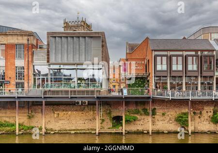 Restaurants an einem Fluss gelegen. Vor den Restaurants befindet sich eine von Rungen gedeckte Terrasse mit Tischen und Stühlen auf der Terrasse. Stockfoto