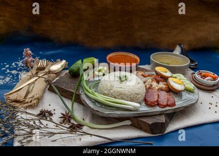 Rotes Schweinefleisch mit Reis (Kao Moo Dang): Rotes Grillpork im thailändischen Stil, Entenei und knuspriger Schweinebauch, geschnittene Gurke mit roter Soße und Brühe. Stockfoto