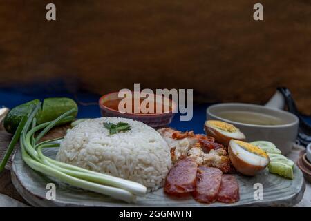 Rotes Schweinefleisch mit Reis (Kao Moo Dang): Rotes Grillpork im thailändischen Stil, Entenei und knuspriger Schweinebauch, geschnittene Gurke mit roter Soße und Brühe. Stockfoto