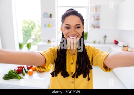 Foto von ziemlich lustig dunkle Haut Dame tragen gelbe Hemd Dreadlocks lächelnd tacking Selfie drinnen Zimmer Haus. Stockfoto