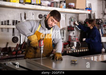 Arbeiter bohren Metallteile mit Handbohrer Stockfoto