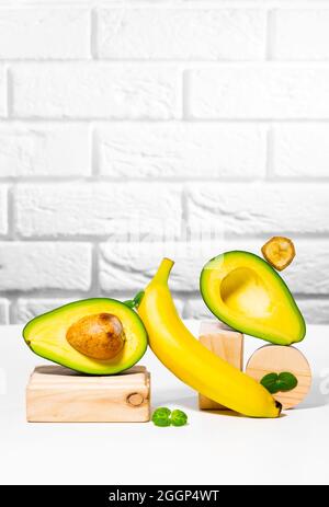 Kreative Avocado, Banane und Micro Green Balance Holzständer und Podien., weißer Hintergrund, Gleichgewicht gesunde Ernährung. Ausgewogenes Ernährungskonzept. Stockfoto