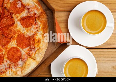 Nahaufnahme offene Box mit Pepperoni Pizza und zwei Tassen Kaffee Espresso auf Holztisch. Draufsicht. Stockfoto