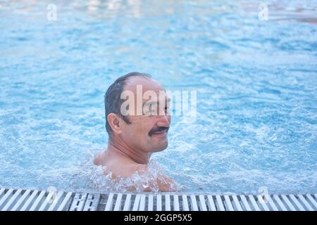 Lächelnder reifer asiatischer Mann im Thermalbecken im Freien mit Hydromassage. Stockfoto