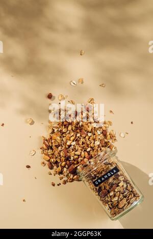 Hausgemachtes Müsli mit Glasglas auf pastellbeigem Hintergrund. Vertikal. Ansicht von oben oder flach liegend. Ästhetisches Hafergranola, schöne Schatten, champagnergelber Hintergrund. Gesundes Frühstückskonzept Stockfoto