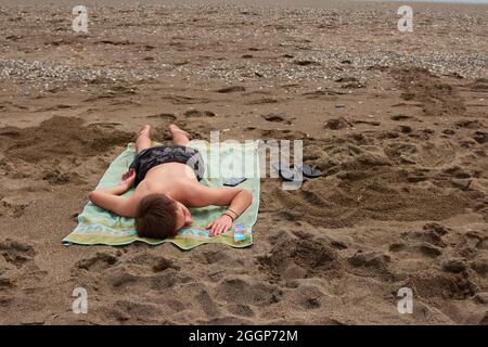 Kaukasischer Mann, der tagsüber auf einem Handtuch am Strand liegt Stockfoto