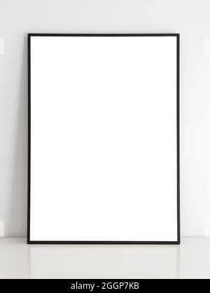Dünner schwarzer imitierter Rahmen auf Tisch mit weißer Wand. Stockfoto