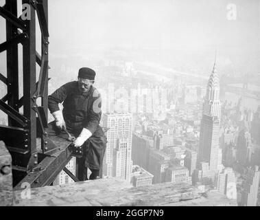 Ein Arbeiter am Rahmen des Empire State Building in New York City, mit dem Chrysler Building im Hintergrund, um 1930. Stockfoto