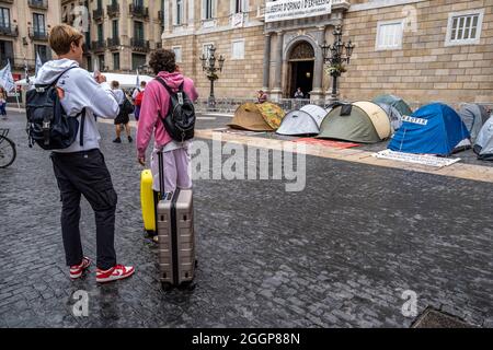 Barcelona, Spanien. September 2021. Touristen mit Koffern werden vor einem Zeltlager gesehen, das während eines Streiks auf der Plaza de Sant Jaume errichtet wurde.am zweiten Tag des Hungerstreiks auf der Plaza Sant Jaume von Geschäftsleuten und Nachtlebenleuten nach dem TSJC (Supreme Court of Justice of Catalonia) Bestätigte die Argumente der Generalitat de Catalunya, das Nachtleben wegen der sogenannten fünften Welle von Covid19 geschlossen zu halten. Kredit: SOPA Images Limited/Alamy Live Nachrichten Stockfoto
