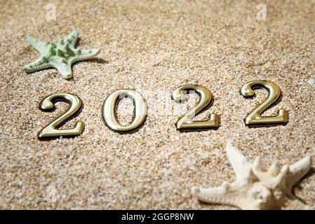 Konzept Strandsaison 2021. Goldene Zahlen 2022 und Seesterne auf dem Sand am Meer. Stockfoto