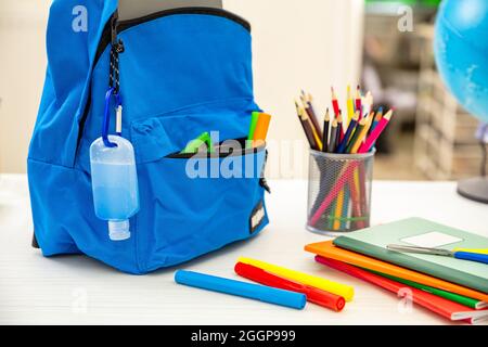 Schule COVID 19 Tage. Coronavirus-Schutzmaßnahme, Händedesinfektionsgel und Rucksack für Schultaschen auf dem Schülerschreibtisch, Nahaufnahme, Stockfoto
