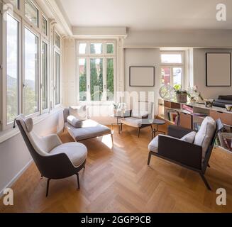 Wohnbereich für Gespräche mit Sesseln und Chaiselongue. Helle Fenster mit Blick auf die Natur. Niemand drinnen Stockfoto