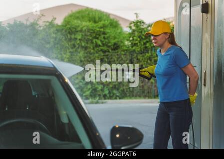 Frau in Uniform Reinigung Auto mit Hochdruckwasser. Autowaschservice. Stockfoto