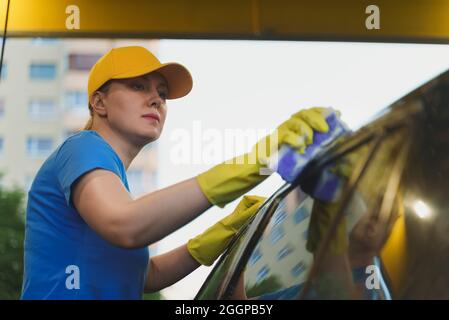 Frau in Uniform Reinigung Auto mit Schwamm. Autowaschservice. Stockfoto