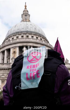 Ein Plakat mit der Aufschrift „REBEL FOR LIFE“ ist an einem Rucksack der Protestierenden festgeklafft, während die Protestierenden am 2. September 2021 von der Tate Modern über die Millennium Bridge während des Extinction Protestes des Rebellions gegen die Massenernagbarung am elften Tag ihrer Impossible Rebellion-Proteste in London, Großbritannien, marschieren. Stockfoto