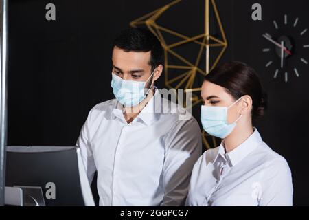 Administratoren in medizinischen Masken, die den Computermonitor an der Rezeption betrachten Stockfoto