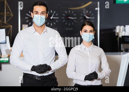 Rezeptionisten mit medizinischen Masken und Latexhandschuhen in der Nähe der Rezeption Stockfoto