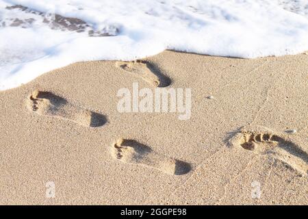 Menschliche Fußabdrücke am Sandstrand mit Meereswellen Stockfoto