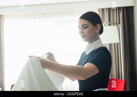 Junge Zimmermädchen in Uniform, die die Bettwäsche im Hotelzimmer umkleiden Stockfoto