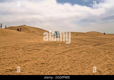 Yazd, Wüste, Iran, 20. Februar 2021:Menschen beobachten, wie ein Offroad versucht, den Sand auf einen Hügel in der Wüste des iranischen Hochlandes gegen den zu klettern Stockfoto