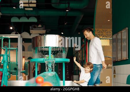 Vater hilft seinem Sohn, auf Wassergeräten im Unterhaltungszentrum zu spielen. Pädagogische Spiele . Tastempfindungen. Emotionen und Freude der Kinder . Arbeiten Stockfoto