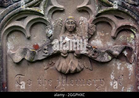 Detail eines alten Grabsteins mit einem Engel, der eine Schriftrolle mit „Sacred“ auf Warwickshire, Großbritannien, hält Stockfoto