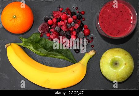 Verschiedene Früchte, Spinatblatt und Glas Smoothie auf schwarzem Steinteller Stockfoto