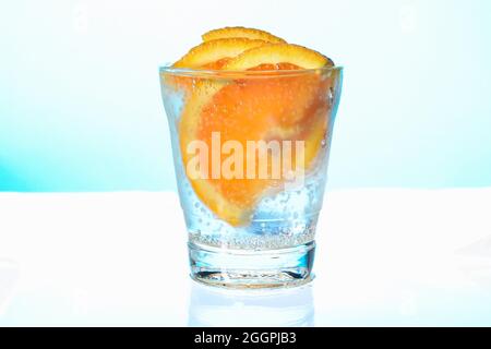 Orangefarbene Scheiben mit Blasen in einem nebelverfärbten Glas mit sprudelndem Wasser Stockfoto