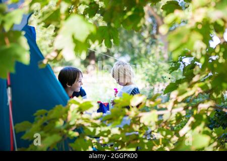 Glückliche Kinder, Frühstück am Morgen vor einem Zelt auf einem Campingplatz im Wald in Norwegen, sonnig am frühen Morgen Stockfoto