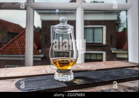 DRAM von Single Malt Scotch Whisky serviert in Probierglas mit Blick auf alte Fenster und Häuser auf gebrauchte Holzkiste Stockfoto