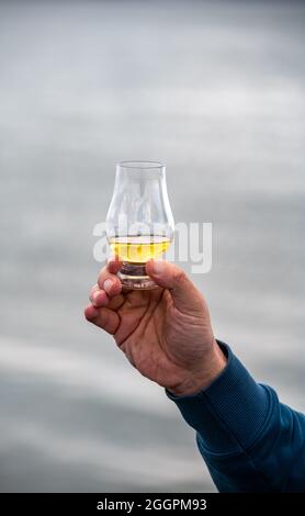 Hand hält einen Schluck Single Malt Scotch Whisky an der Küste In Schottland Stockfoto